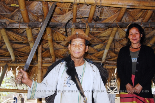 Capo villaggio ADI GALLONG con cappello di bambù intrecciato con la tesa appuntita, il machete a tracolla ed il gilet/corazza di fibra vegetale